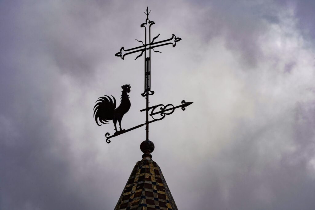 Veleta met&aacute;lica en el tejado de una casa recortada contra un cielo nublado