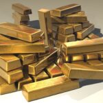 Lingotes de oro apilados sobre una superficie metálica bajo una luz fría de almacén
