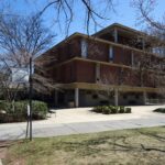 Edificio universitario de ladrillo con ventanas altas y varios estudiantes cruzando la entrada