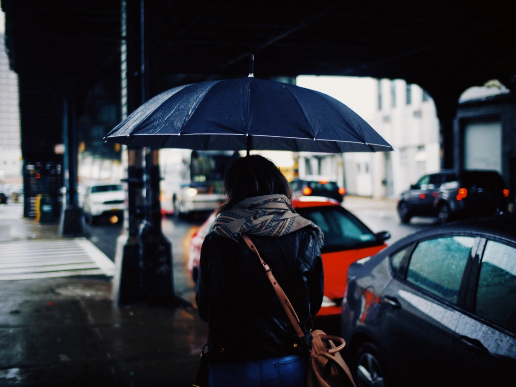 Paraguas oscuro abierto bajo la lluvia en una acera con charcos y reflejos