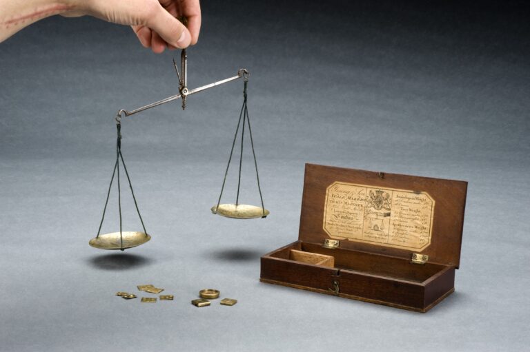 Balanza antigua de latón con dos platillos y varias pesas colocadas sobre una mesa