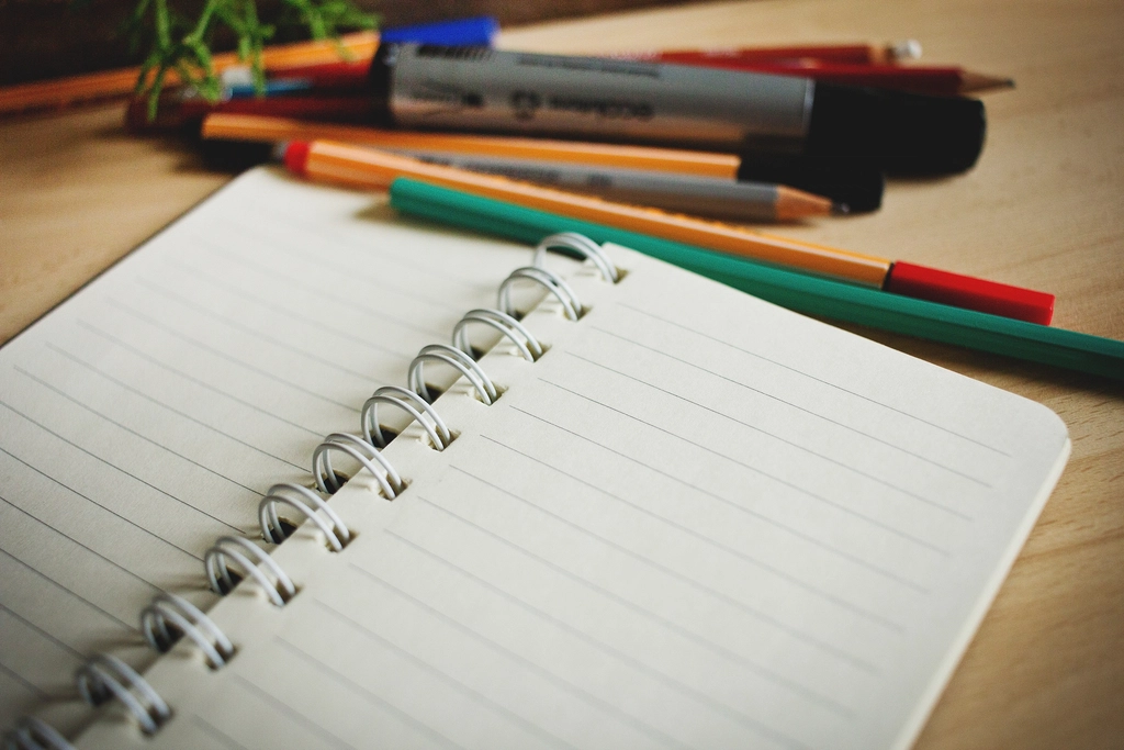 Cuaderno abierto con un l&aacute;piz encima sobre un escritorio junto a una taza de caf&eacute;