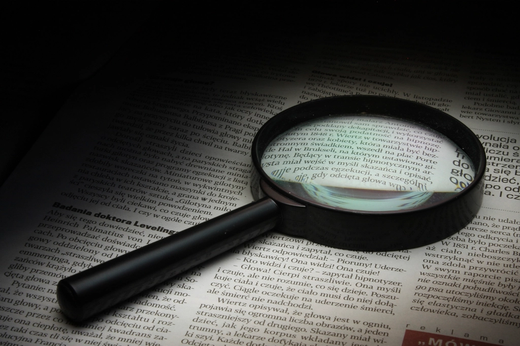 Lupa apoyada sobre un documento impreso con p&aacute;rrafos de letra peque&ntilde;a